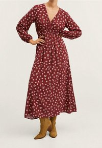 Vínové maxi šaty s bílým květinovým vzorem, dlouhými rukávy, výstřihem do V a elastickým pasem. Kombinované s špičatými koženými kotníkovými botami ve světle hnědé barvě.