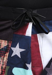 Flerfärgade badshorts med ett lapptäcktsdesign och svart dragsko. Den texturerade tyget inkluderar mönster av stjärnor och rutmönster.