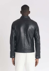 Veste en cuir noir avec un design ajusté, coutures visibles et accents de boutons-pression. Présente un col montant et des manches longues.