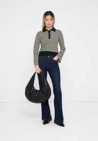 Striped long-sleeve top with a black collar, paired with dark denim flared jeans. Model holds a large, soft black hobo bag.