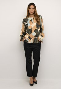 Blusa astratta multicolore con maniche ampie, scollo con bottoni, abbinata a pantaloni neri aderenti e scarpe nere a punta.