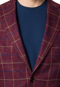 Burgundowa marynarka w kratę z niebieskimi i złotymi liniami, z wyciętym kołnierzem i jednym czarnym guzikiem, na granatowej koszulce.