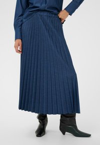 Sötétkék, pliszírozott maxi szoknya elasztikus derékrésszel, texturált anyagból készült, fekete bokacsizmákkal párosítva, hegyes orral.