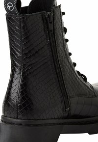 Bottine noire avec une finition texturée en motif reptile. Elle présente une fermeture éclair sur le côté, un la�çage à l'avant et une semelle épaisse noire.