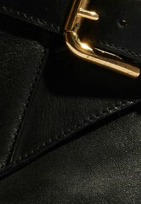 Czarna skórzana torba z geometrycznym wzorem i wyraźnym zapięciem w złotym odcieniu. Powierzchnia ma gładką teksturę z subtelnymi detalami przeszycia.