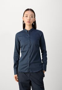 Camicia blu navy con bottoni, colletto classico, maniche lunghe, tessuto liscio e lucentezza sottile; presenta bottoni scuri e vestibilità sartoriale.
