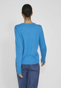Pull tricoté bleu avec un col rond, des poignets et un ourlet côtelés ; associé à un jean en denim foncé, vu de dos.