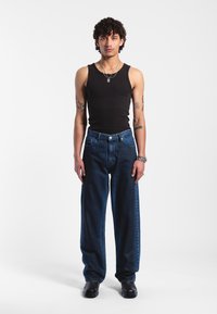 Černé tílko, volné tmavě modré džíny, kožené boty. Mezi nápadnými detaily patří opasek s kovovými prvky a vrstvené náhrdelníky.