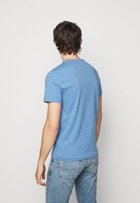 Blue short-sleeve t-shirt made of textured cotton fabric. Rounded neckline and a relaxed fit, paired with light blue denim jeans.