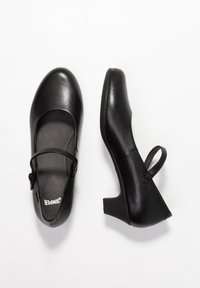 Črne usnjene Mary Jane čevlje s zaobljenim nosom, nastavljivo zanko in srednjim blokastim peto. Gladka tekstura z minimalnim okrasjem.