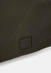 Sac en cuir vert foncé avec un design matelassé, présentant des coutures visibles et un patch de logo embossé. Texture lisse avec un éclat subtil.