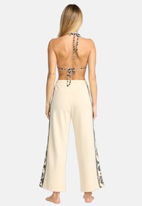 Top halter con patrón en blanco y negro con cierre de lazo, combinado con pantalones de talle alto en color crema que presentan una impresión gráfica lateral.