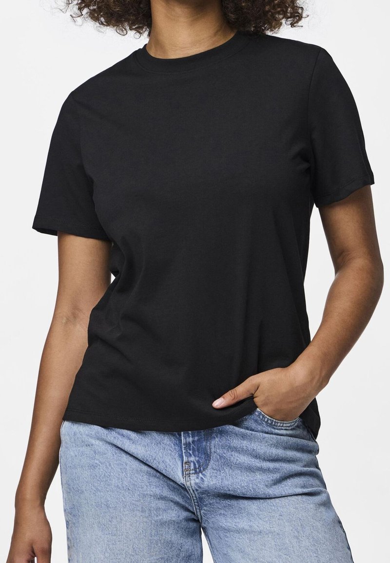 T-shirt en coton noir à manches courtes, col rond et coupe décontractée, associé à un jean en denim bleu clair. Design simple et polyvalent.
