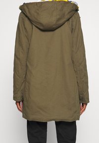 Parka verde oliva con capucha, que presenta textura acolchada, un dobladillo ligeramente curvado y un forro de forro polar colorido en el cuello.