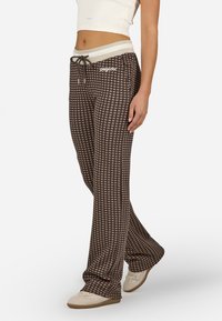 Brūnas svītrainas bikses ar aukliņu jostas daļā, ar beigu režģa dizainu smilšu krāsā un mīkstu audumu. Valkā ar gaišām kurpēm.