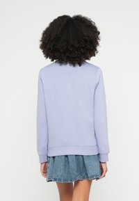 Violets violetā džemperis ar apaļu apkakli, ribotu aproču un apakšmalu. Kombinēts ar džinsa svārkiem, kas atspoguļo slāņainu tekstūru un ikdienišķu stilu.