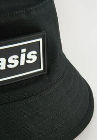 Mustaharja musta ämpärilätsä, joka on valmistettu teksturoidusta kankaasta ja jossa on suorakulmainen kumitarra, jossa on sana "Oasis" vahvoilla valkoisilla kirjaimilla.
