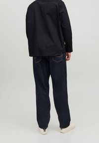 Camicia nera a maniche lunghe con taglio dritto, abbinata a jeans in denim blu scuro a vestibilità ampia e sneakers bianche. Design semplice e funzionale.