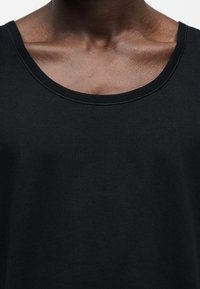 Gros plan d'une personne portant un t-shirt noir à encolure dégagée, montrant la clavicule et le haut de la poitrine.