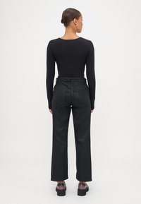 Top negro de manga larga combinado con jeans de tiro alto y pata ancha negros, que cuentan con una textura suave y bolsillos traseros estructurados. Zapatos negros completan el conjunto.