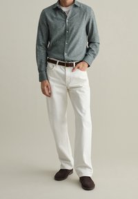 Camicia grigia a maniche lunghe con texture, jeans bianchi a gamba dritta, cintura in pelle marrone e scarpe marroni scure. Design semplice e colori neutri.