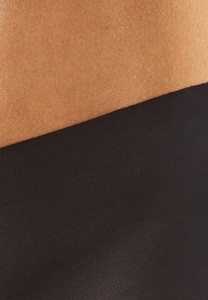 Lähikuva vaaleanruskeasta ihosta mustan vaatteen vyötäröriman yläpuolella, näyttäen sileän pinnan ja kangasdetailin.