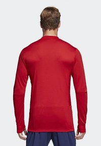 T-shirt de sport rouge à manches longues avec col rond, coupe ajustée et tissu lisse. Présente un ourlet plat sans logos ni motifs visibles.