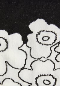 Tessuto in bianco e nero con un motivo floreale caratterizzato da petali contornati e centri circolari, che mette in risalto una morbida texture lavorata a maglia.