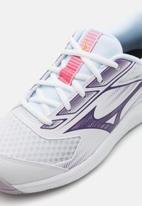 Hvid sportssko med lilla accenter og mesh tekstil. Har en polstret tunge, hvide snørebånd og en tekstureret sål.
