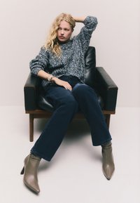 Suéter de punto con un patrón texturizado y multicolor, combinado con pantalones de mezclilla oscuros de pierna ancha y botines taupe con punta y correa.