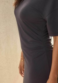 Robe gris foncé au design ajusté, texture douce et détail de ruching sur le côté. Manches courtes et style minimaliste.