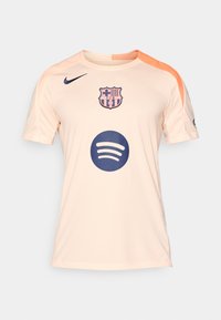 Licht perzikkleurig voetbalshirt met korte mouwen, met een marineblauwe clubembleem en Spotify-logo, plus een oranje accent op de schouder.