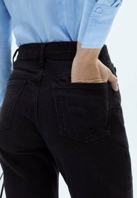 Črne jeans hlače iz denima z visokim pasom in dvema zadnjima žepoma. Svetlo modra srajca je vtaknjena notri, kar razkriva območje žepov.