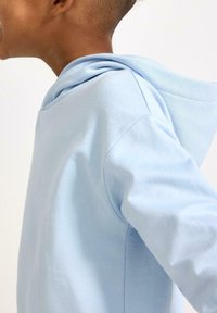 Hellblauer Hoodie aus weichem Stoff, mit entspannter Passform und einer eng anliegenden, abgerundeten Kapuze. Das Design umfasst lange Ärmel und eine nahtlose Schulter.