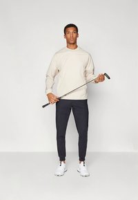 Šviesiai smėlio spalvos marškiniai ilgomis rankovėmis derinami su tamsiomis kelnėmis, laikoma golfo lazda. Baltos sportinės avalynės, paprasto dizaino, be matomų raštų.