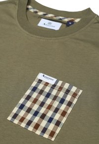 T-shirt verde olivo con una tasca a quadri in contrasto nei colori marrone, blu e avorio. Collo rotondo e dettaglio dell'etichetta tessuta all'interno del colletto.