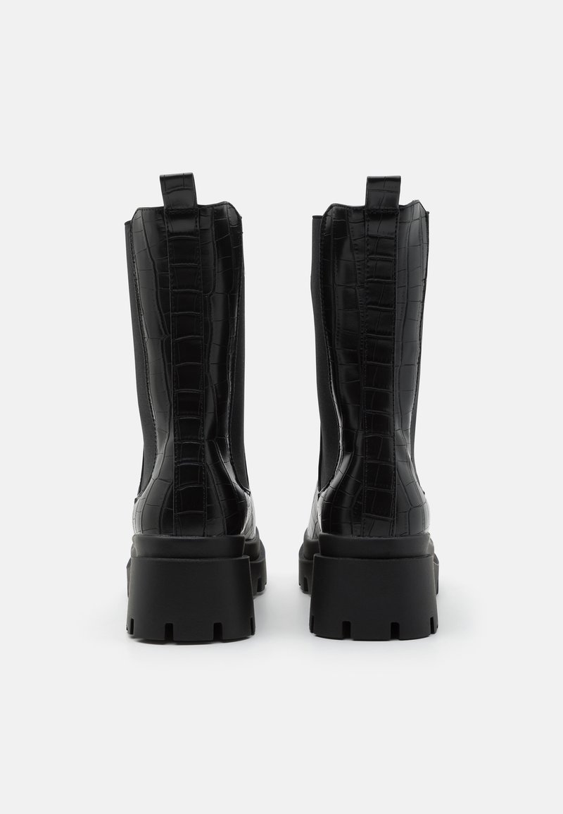 Stivali alla caviglia neri con un motivo texturizzato simile a quello del coccodrillo, suola spessa e linguetta sul retro per facilitarne l'indossamento.
