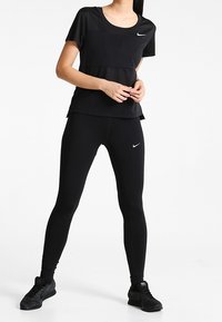 Ropa deportiva negra compuesta por una camiseta ajustada y leggins, con un logotipo de Nike, textura suave y un diseño aerodinámico.