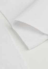 Weißer Stoff mit glatter Textur und weichem Finish, mit einer gefalteten Kante. Das Material scheint leicht und mit subtilen Rippenstrukturen versehen zu sein.