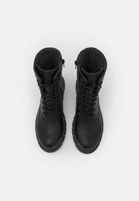Botas de tobillo negras de cuero con un forro texturizado gris. Incluyen cordones, una punta redondeada y una suela de goma gruesa.