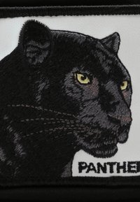 Toppa con la testa di un pantera nera, ricamata con dettagliati effetti di pelliccia, occhi gialli e la parola "PANTERA" in basso su uno sfondo bianco.