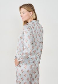 Camisa de pijama con estampado floral y rayas verticales. Mangas largas, cuello botonado, hecha de una tela ligera en suaves tonos pastel.