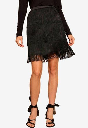 Czarna spódnica z frędzlami o warstwowej fakturze, z prostym dołem i dopasowanym pasem. Połączona z czarnymi sandałami na paski.