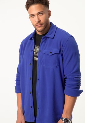 Blue fleece shirt jacket with button closure, single chest pocket, and rolled cuffs. Worn over a black graphic t-shirt.