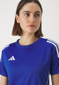Blauw sport T-shirt met korte mouwen, gemaakt van glad materiaal, met witte accentstrepen op de schouders en een logo op de borst.