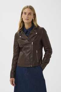 Giubbotto biker in pelle marrone con tasche con zip e colletto a scatto; abbinato a una camicia di jeans blu sotto. Tessuto liscio e design aderente.