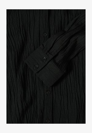 Czarna, pomarszczona koszula z guzikiem, wykonana z teksturowanej tkaniny, z długimi rękawami oraz czarnymi guzikami przy mankietach i na przodzie.