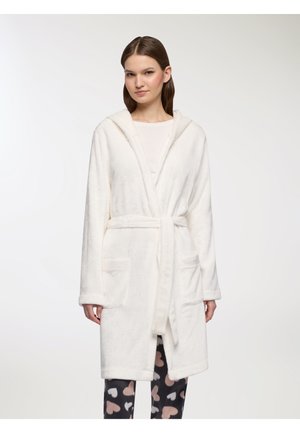 Accappatoio bianco con cappuccio realizzato in tessuto morbido, dotato di cintura da annodare e due tasche frontali. Abbinato a pantaloni scuri decorati con cuori di colore chiaro.