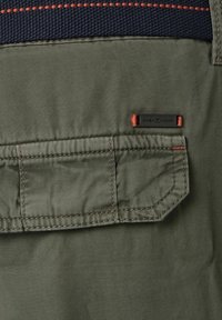 Olivgrüner Stoff mit einem strukturierten marineblauen Panel und orangefarbener Naht. Enthält ein Patch-Label, das unten rechts "CASA MODA" liest.