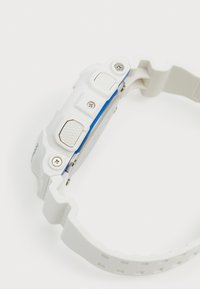 Montre en résine blanche avec un accent bleu et des boutons texturés. Elle dispose d'un bracelet moulé durable et de vis visibles sur le côté.